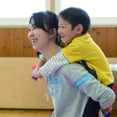 笑顔の関向さん親子（子をおんぶする関向さん）の画像